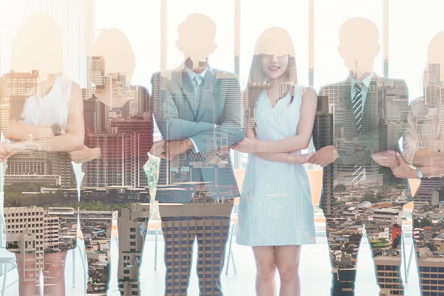 Commercial Insurance - Professionals Standing and Holding Hands in an Office with Reflected Image of a City Landscape That Appears Over The Professionals