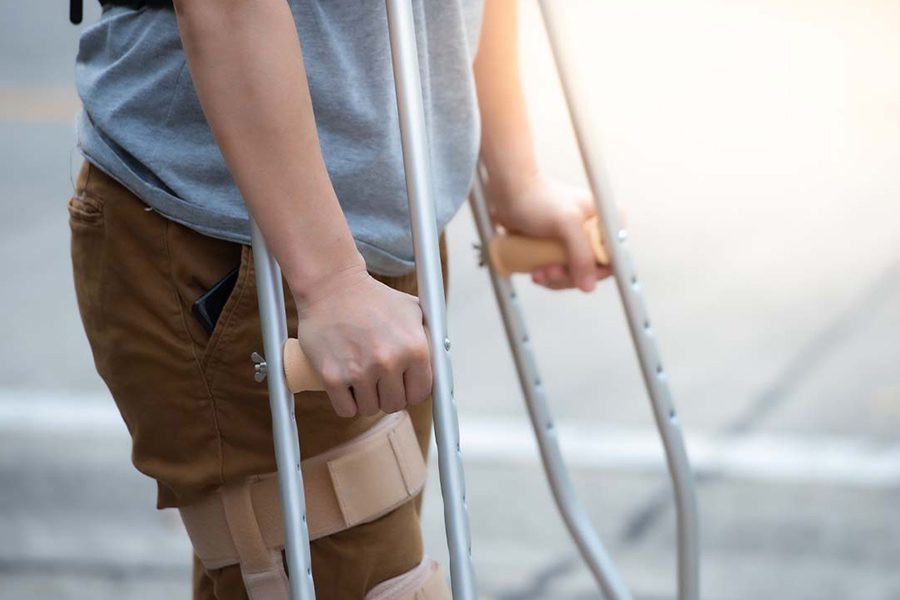 Disability Insurance - Close Up of Womans Lower Body and Knee Support Using Crutches Standing and Trying to Walk After Suffering a Work Related Injury